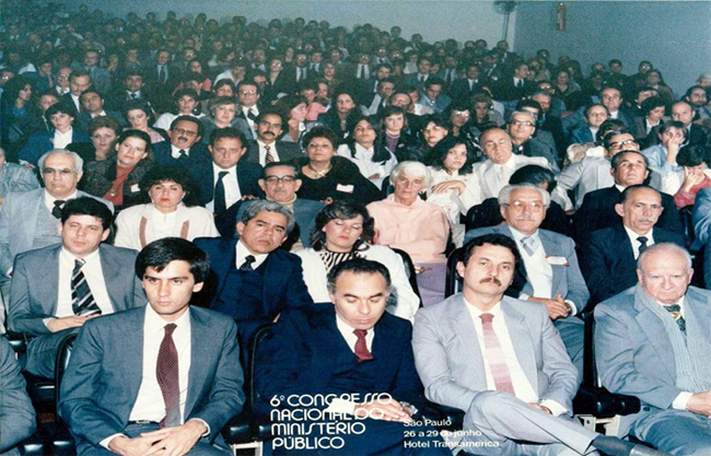 uma dimensão de aproximadamente 200-300 pessoas sentadas em um auditório, de frente para a câmera