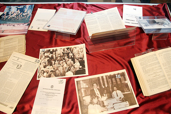 em cima de um pano vermelho, duas fotos antigas com pessoas e diversos papeis e documentos (ilegíveis)