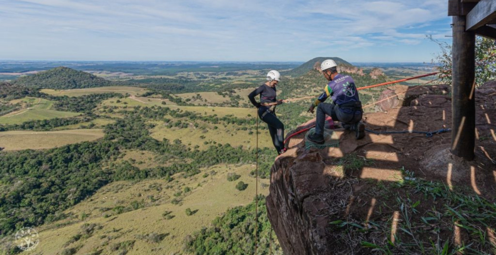 instrutor orienta mulher na beira de uma pedra a descer o barranco com corda